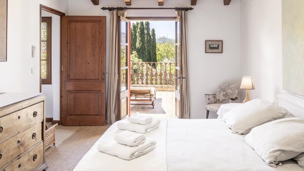 Un dormitorio con techo de madera, una cama con almohadas, un aparador y vistas a un balcón con barandilla.