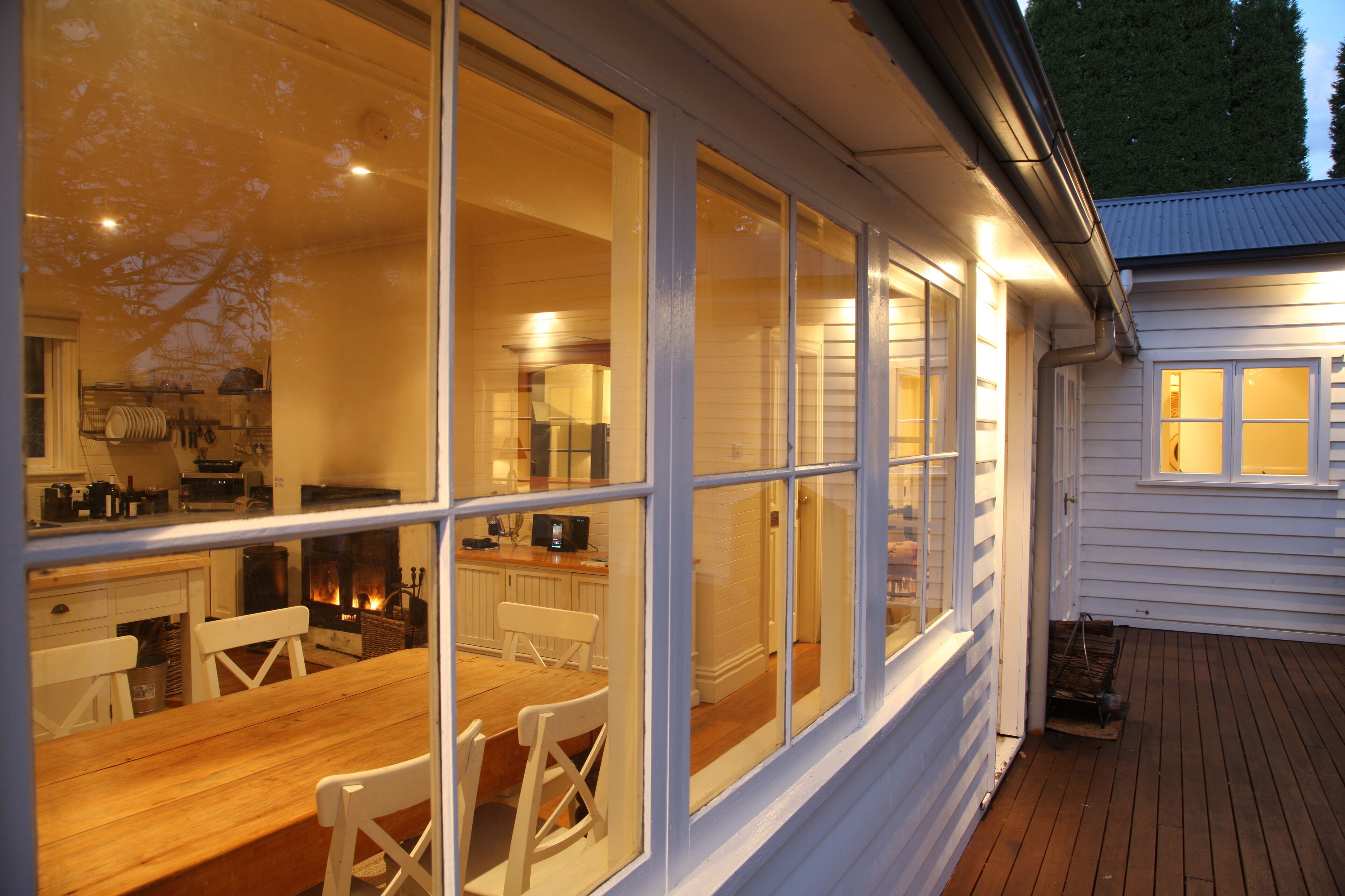A cozy interior with a wooden dining table and chairs, large windows, and a visible kitchen area.