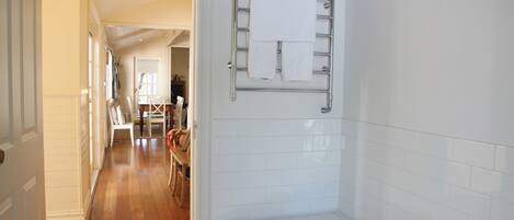 A bathroom with a bathtub, a towel rack, and a wooden floor leading to a dining area.