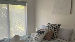 Un letto rifatto con cura, una coperta a righe, un asciugamano arrotolato e diversi cuscini decorati. Sopra il letto, un'opera d'arte a forma di foglia.