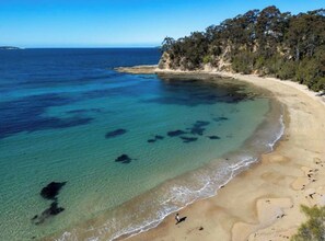 A beach with clear water, a sandy shore, and a forested cliff. - 80m to the sand Sunshine Bay Retreat, Bateman’s Bay (Sunshine Bay)