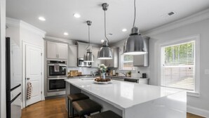 A modern kitchen with white cabinetry, a large island with bar stools, stainless steel appliances, and pendant lighting.