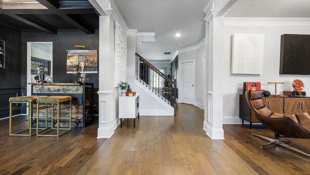 A spacious living area with a wooden floor, a staircase, and a bar area with stools.