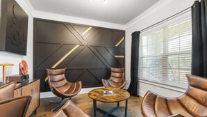 A modern living room with leather armchairs, a round coffee table, and a geometric accent wall.