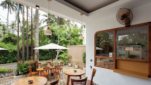 An outdoor café with wooden tables and chairs, surrounded by lush greenery and a view of the street. - Merta Luwih villa (Tabanan)