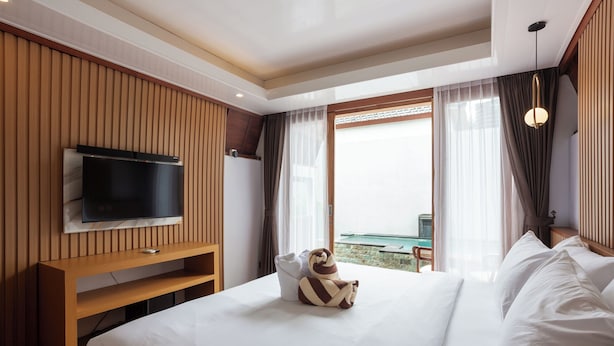 A hotel room with a bed, a TV mounted on a wooden panel wall, a balcony with a view, and a hanging light fixture. - Merta Luwih villa (Tabanan)
