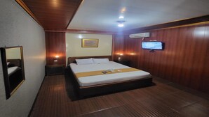 Une chambre d’hôtel avec un lit en bois, une télévision, une table de chevet et un miroir.