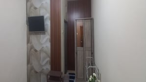 Un couloir avec un mur recouvert de panneaux de bois, un téléviseur fixé au mur, une porte en métal et une petite marche menant à une pièce.
