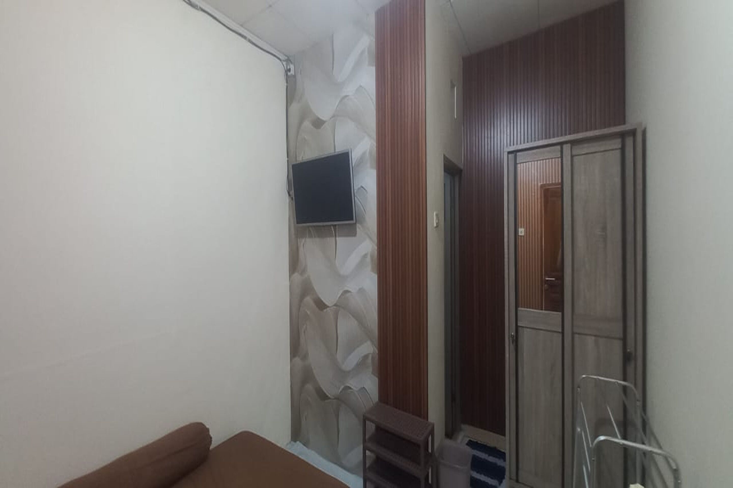 A room with a bed, a TV mounted on the wall, a wardrobe, and a small table.