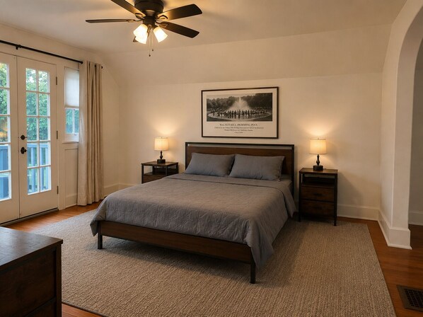 A bedroom with a bed, two bedside tables, a ceiling fan, a framed picture on the wall, and a door with curtains. - Historic Omaha Home overlooks Park. 3BR. Free Parking. 2.7 miles to Schwab Field (Omaha)