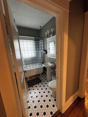 A bathroom with a bathtub, sink, and toilet, featuring a hexagonal tile floor and a shower curtain. - Historic Omaha Home overlooks Park. 3BR. Free Parking. 2.7 miles to Schwab Field (Omaha)