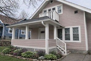 A two-story house with a covered porch, a stone foundation, and a garden with various plants. - Historic Omaha Home overlooks Park. 3BR. Free Parking. 2.7 miles to Schwab Field (Omaha)
