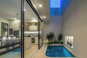 Une cuisine moderne avec une porte en verre donnant sur un coin repas, une petite piscine intérieure et un mur décoratif agrémenté de vases.
