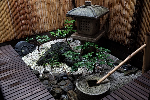 A traditional Japanese garden with a stone lantern, bamboo wall, and a wooden walkway.