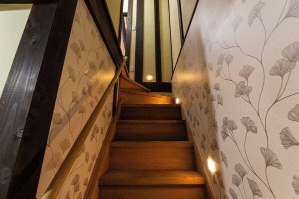 Un escalier en bois, avec un papier peint à motifs floraux de chaque côté.