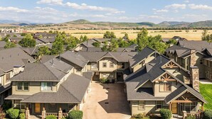 Un barrio residencial con varias casas de techo a dos aguas y chimeneas de piedra, rodeado de campos abiertos y colinas distantes.