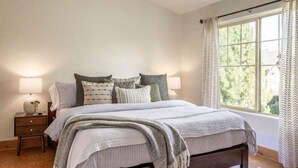 Un dormitorio con una cama grande, dos mesitas de noche y una ventana con cortinas.