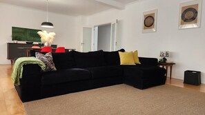 Ein Wohnzimmer mit einem schwarzen Modulsofa, einem roten Sessel, einem kleinen Tisch mit Pflanze und einem großen Gemälde an der Wand.