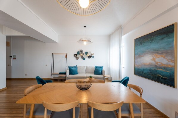 Un salon moderne avec une table à manger en bois, un canapé agrémenté de coussins bleus, un luminaire suspendu et un grand tableau abstrait accroché au mur.