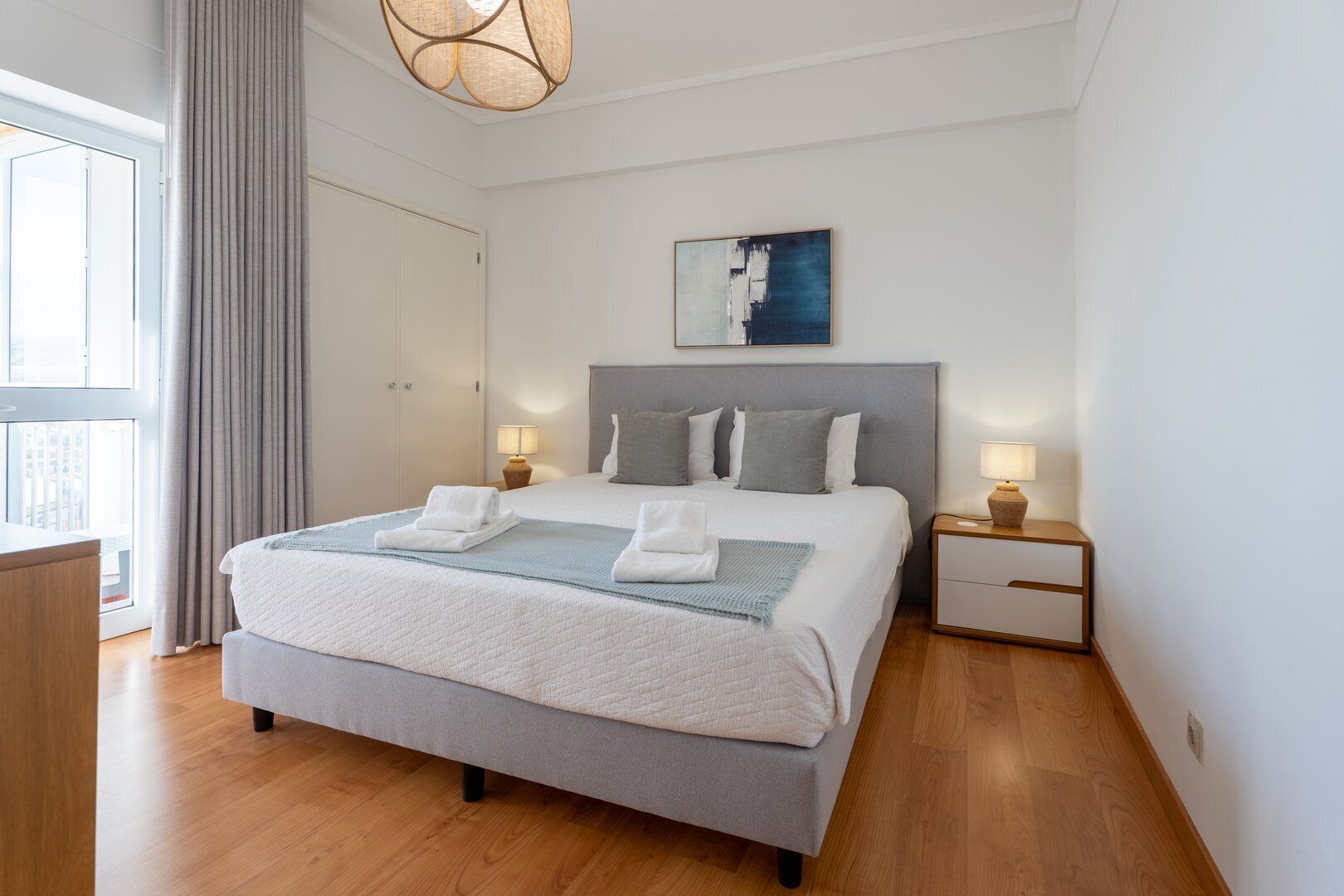 Ein modernes Hotelzimmer mit einem großen Bett, Nachttischen, einem Bild an der Wand und einem Fenster mit Vorhängen.