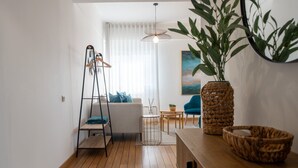 A modern living room with a wooden floor, a sofa, a coffee table, a hanging light fixture, and a large plant. - Solmar Sunset Place | Marina View (Ponta Delgada)
