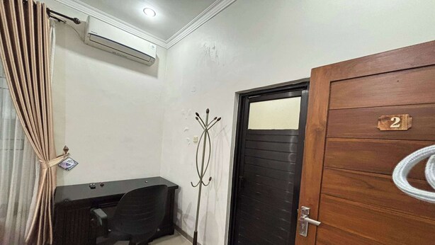 A room with a desk, chair, and a coat rack. There is a door with a number plate and a coiled cable on the floor. - OYO 95075 Matoorstay Syariah (Pogung Lor)