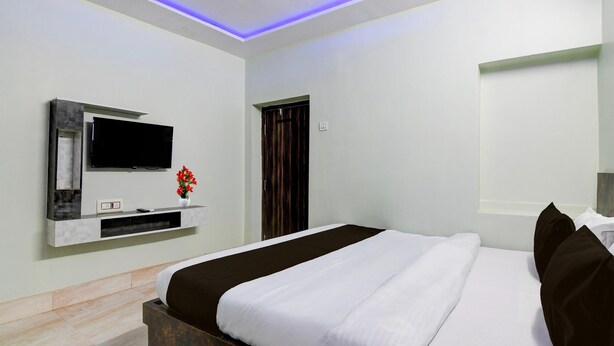 A modern hotel room with a large bed, a flat-screen TV mounted on a wall, and a small table with a vase of flowers. - Hotel O Chinar Park Kolkata Zapper (Barasat)