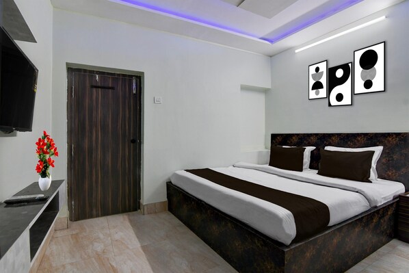 A modern bedroom with a large bed, a flat-screen TV, a vase with red flowers, and abstract wall art. - Hotel O Chinar Park Kolkata Zapper (Barasat)