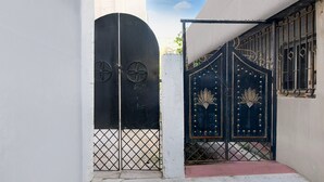 A black gate with decorative metalwork, a white wall, and a window with bars. - Hotel O Chinar Park Kolkata Zapper (Barasat)