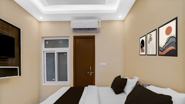 A hotel room with a bed, a TV mounted on the wall, an air conditioning unit, a window, and artwork on the wall. - Hotel O Deva Road Lucknow Awadh Regency (Lucknow)