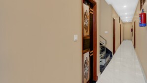 A long, narrow hallway with beige walls, a marble floor, and a fire extinguisher mounted on the wall. - Hotel O Deva Road Lucknow Awadh Regency (Lucknow)