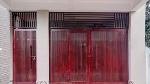 A red metal gate with vertical bars and a small window, leading to a building with a tiled entrance and steps. - Hotel O Deva Road Lucknow Awadh Regency (Lucknow)