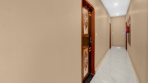 A hallway with beige walls and a marble floor, leading to a door with a decorative panel. - Hotel O Deva Road Lucknow Awadh Regency (Lucknow)