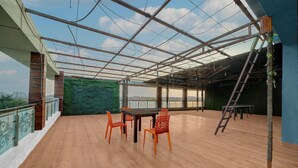 A spacious indoor area with a wooden floor, a table with chairs, a green wall, and a view through a glass ceiling. - Collection O Bhel Piplani Bhopal (Bhopal)