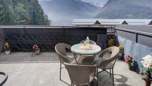 Un balcon agrémenté de meubles en osier, d’une table en verre et de plantes en pot.