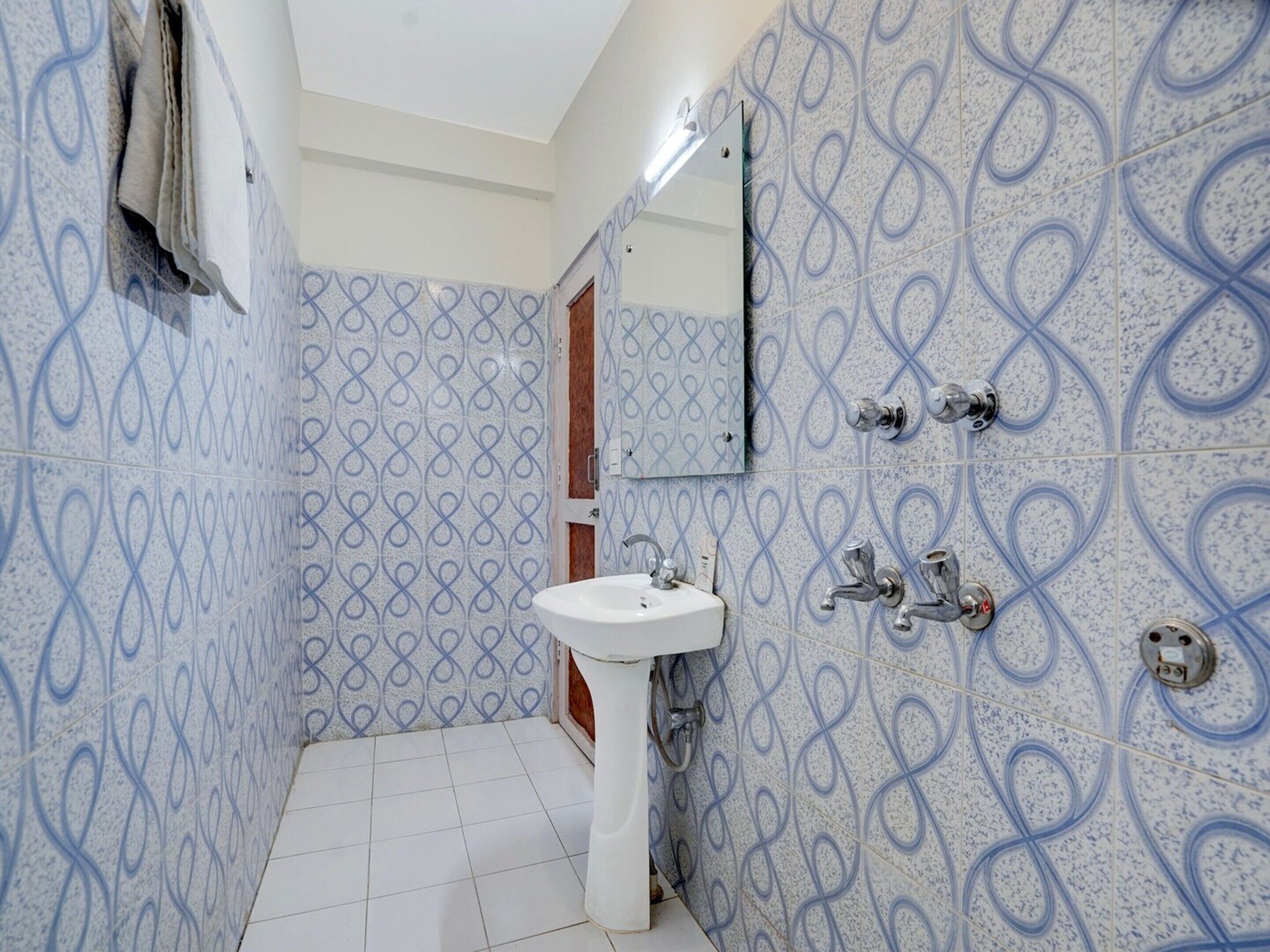 Een badkamer met een wit wastafelmeubel, twee kraanwerk en een spiegel. De wanden hebben een blauw-wit patroon.