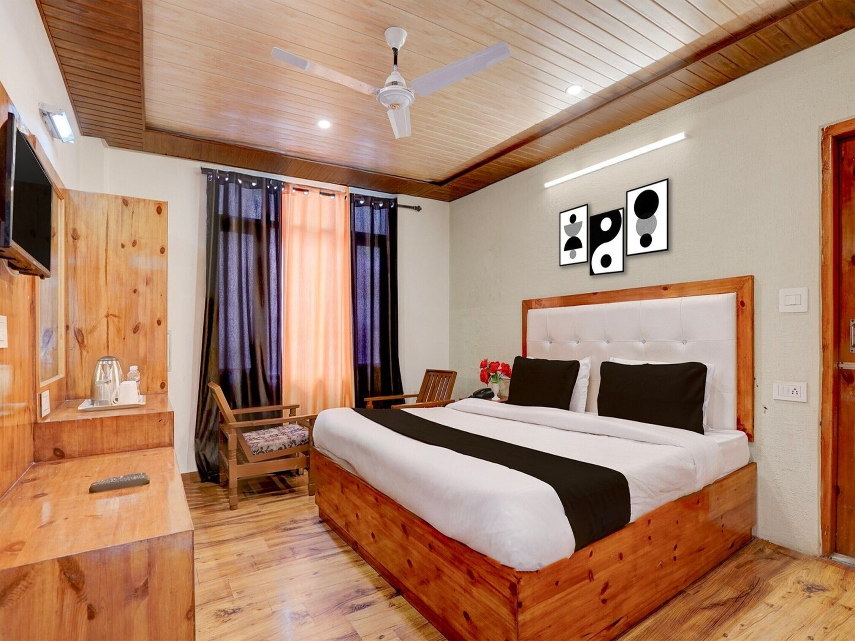 Un dormitorio con una cama de madera, ventilador de techo, televisión y escritorio con hervidor.