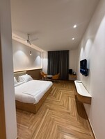 A modern hotel room with a large bed, a desk, a chair, a television, and a ceiling fan.