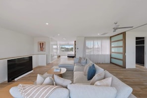 A modern living room with a flat-screen TV, a sofa set, a coffee table, and a large window with curtains. - Dune House (Tweed)