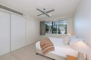 Ein Schlafzimmer mit einem Bett, einem Deckenventilator, einem Fenster mit Vorhängen und Blick auf Grünfläche.