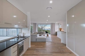 A modern kitchen with a dining area, a sofa, and a view of the outdoors. - Dune House (Tweed)