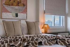A bedroom with a bed, pillows, a blanket, a lamp, and a painting on the wall. - Dune House (Tweed)