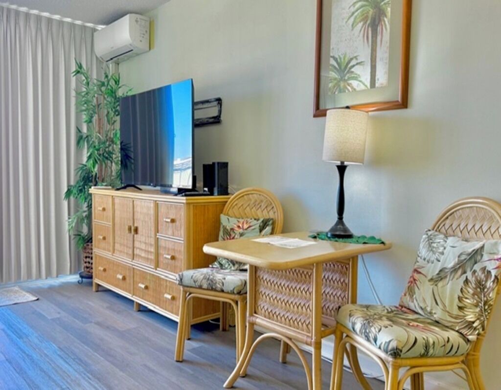 A room with a television, a table, two wicker chairs, a cabinet, and a plant. - Island-Inspired Cozy Retreat - Free WIFI (Honolulu)