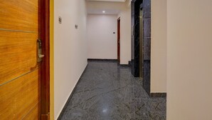 Un couloir avec une porte en bois sur la gauche, un sol en marbre et un mur en marbre noir sur la droite.
