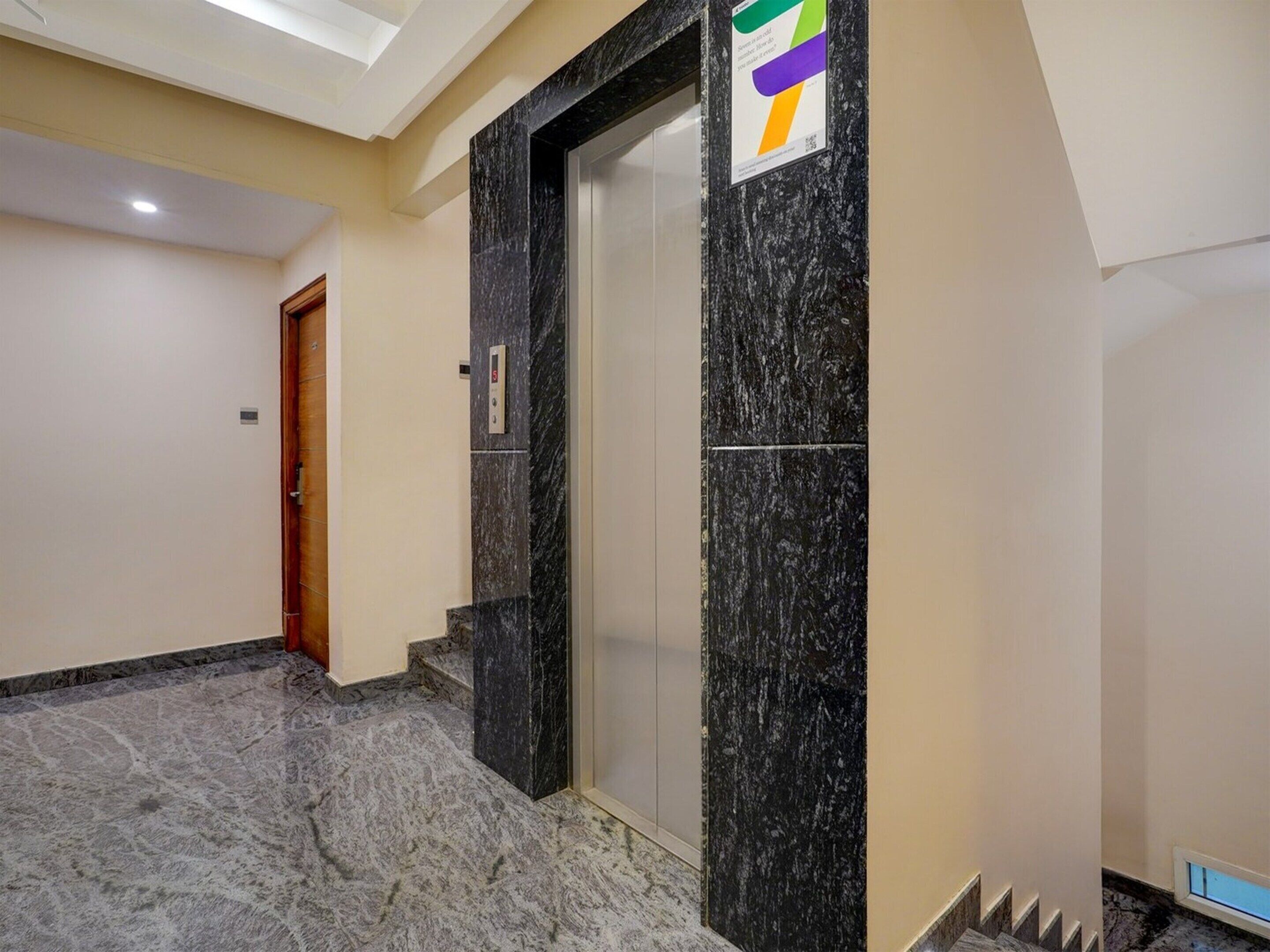 Passadís amb sòl de marbre, una porta i panell de control d'ascensor fixat a la paret.