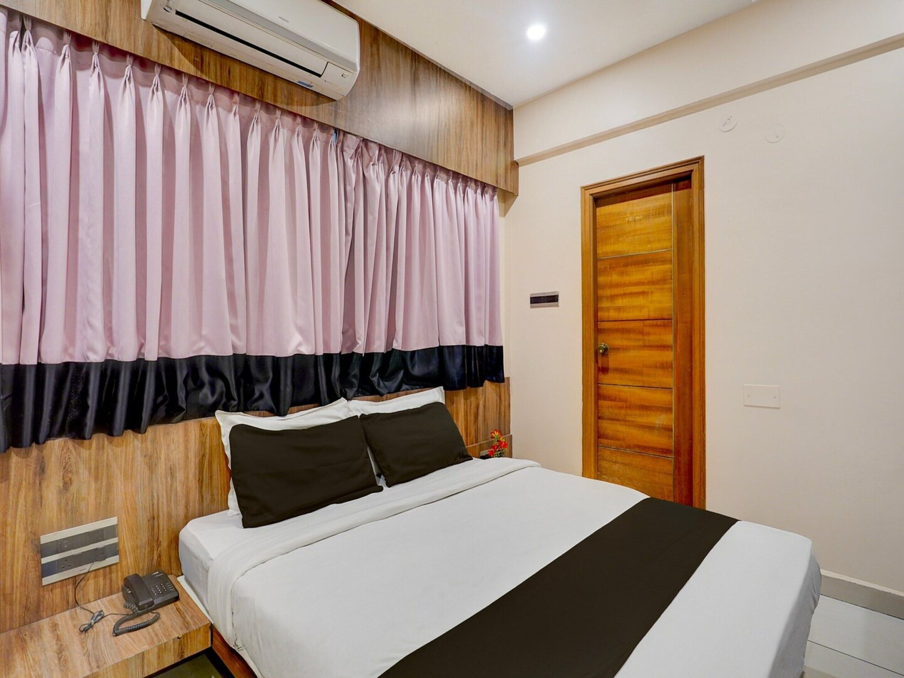 A hotel room with a bed, a wooden headboard, a telephone, and an air conditioning unit.