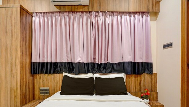 Une chambre à coucher avec une tête de lit en bois, un lit recouvert d’une literie blanche, deux oreillers noirs et un rideau rose et noir.