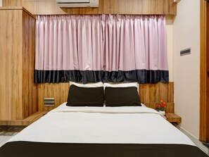 Una camera da letto con una testiera in legno, un letto con biancheria bianca, due cuscini neri e una tenda bicolore rosa e nera.