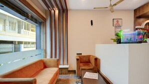 Un hall d’hôtel moderne avec un canapé, des fauteuils, un comptoir d’accueil et un ventilateur de plafond.