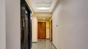 Un couloir d’hôtel avec un sol en marbre, une porte en bois au fond et un luminaire au plafond.